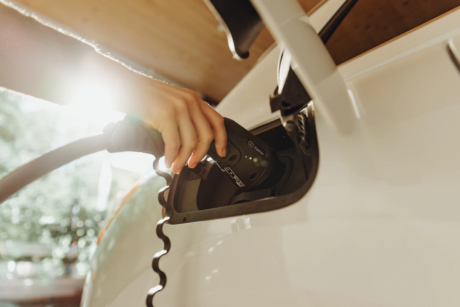 A hand plugging a charging cable into a white electric car