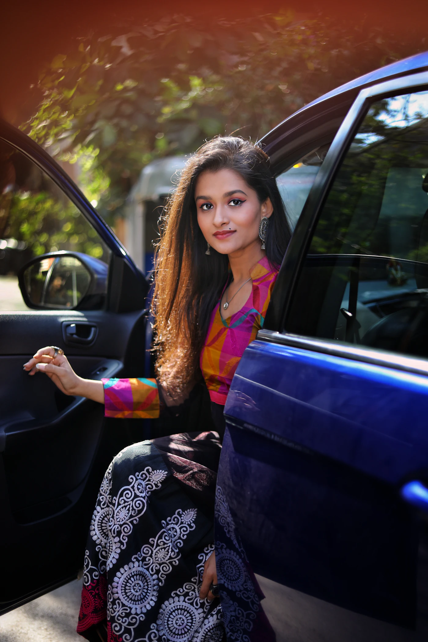 A smiling woman in a colourful tunic at the open door of a car